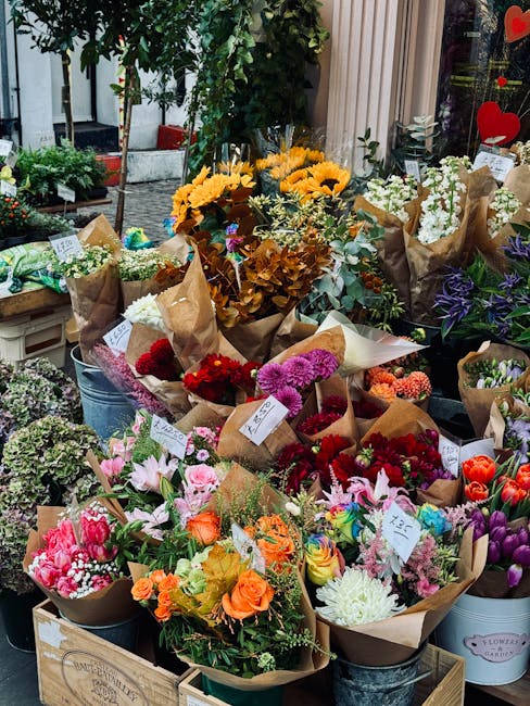 A vibrant display of freshly cut flowers arranged in various bouquets at a florist shop. The arrangements include a mix of roses, tulips, chrysanthemums, and lilies in vivid colors such as pink, orang