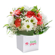 Radiating a joyful exuberance akin to a walk through Spitalfields' bustling lanes, this floral arrangement exudes freshness and charm. Lush coral, peach, and crimson carnations, awash in softness and ruffled detail, nestle comfortably with white daisies whose lively green centres bring a pop of energy to the bouquet. Wispy baby's breath drifts through the blooms, casting a light, airy veil across the arrangement reminiscent of morning mist over Spitalfields Market rooftops. Peeking from one side, dainty, unopened blooms-touched with hints of purple-introduce a playful sense of anticipation and creativity. Enveloping the entire display, broad, glossy leaves impart resilience and fullness, their rich texture reminiscent of the leafy enclaves near Brick Lane parks. The bouquet is thoughtfully set in a square white gift bag, with white ribbon handles looping over for easy carrying. Meticulously arranged and bursting with visual delights, the ensemble feels at home in the vibrant, diverse community of Spitalfields-ideal for celebratory gifting, brightening up a workspace, or surprising a loved one with a piece of local artistry and joy.